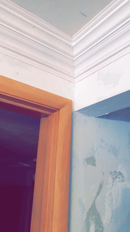 Corner of a room with white crown molding, a wooden door frame, and a blue wall with peeling paint.