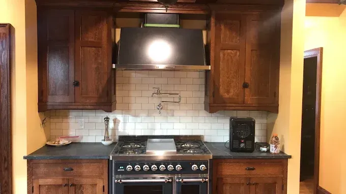 Wooden kitchen with a stove, cabinets, stainless range hood, and small appliances on the countertop.