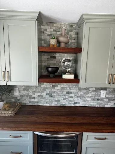 Kitchen with white cabinets, dark wood countertop, mosaic backsplash, and open shelves with decor.