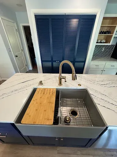 Kitchen island with farmhouse sink, wood cutting board, and brass faucet in front of blue cabinets.