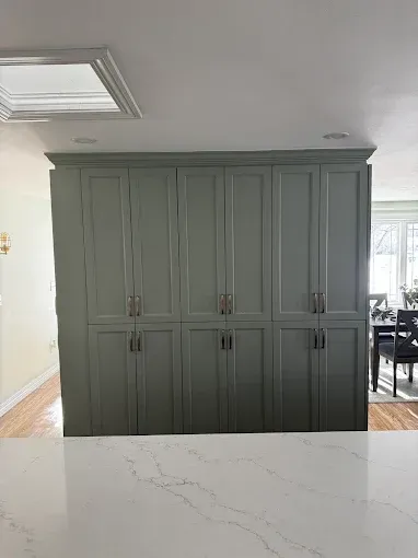 Gray built-in cabinets with paneled doors in a bright kitchen, seen behind a white marble island.