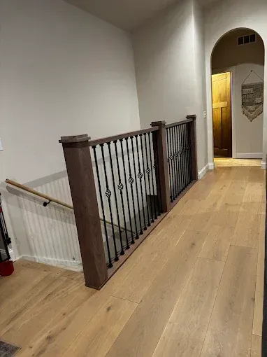 Interior hallway with wood floor, black stair railing, and an arched doorway ahead