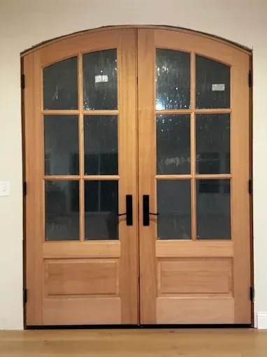 Double wooden French doors with black handles and glass panes in a beige wall