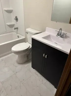 Small bathroom with bathtub, toilet, and black vanity with sink and mirror.