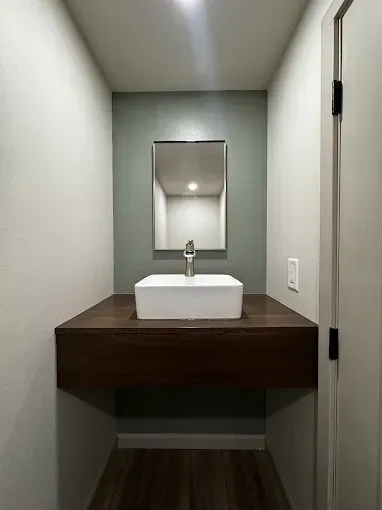 Narrow bathroom with a white sink on a dark wood vanity and a mirror in a small alcove.