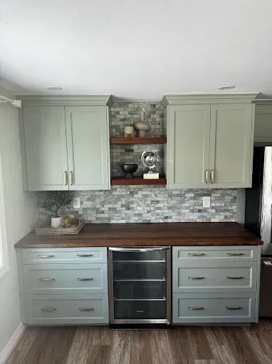 Gray kitchen cabinets and island with dark wood countertop and stone backsplash, centered around a stainless oven.