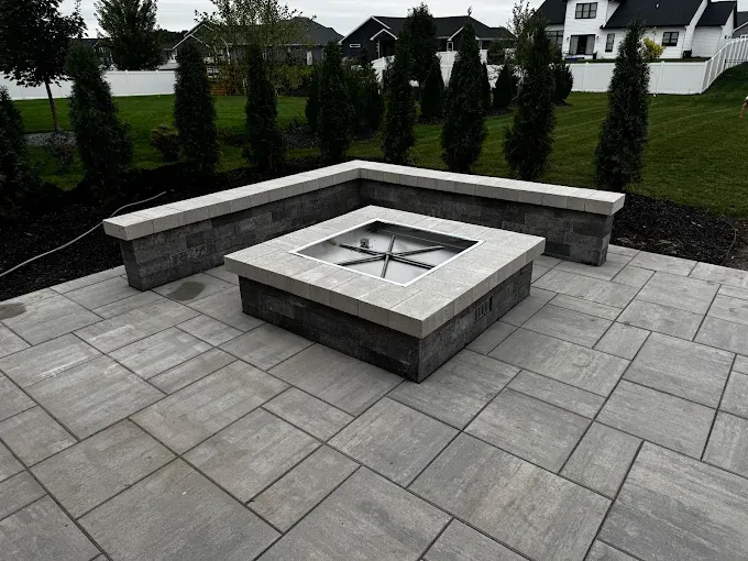 Stone patio fire pit with built-in bench seating in a landscaped backyard