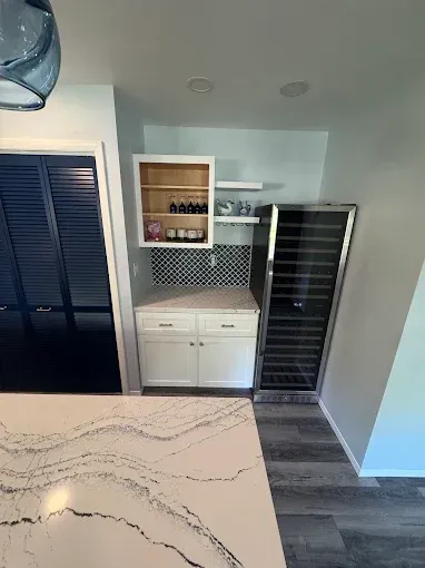 Kitchen nook with white cabinets, open shelves, wine fridge, and black shutter doors beside an island countertop