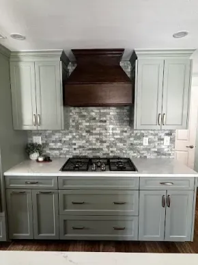 Modern kitchen with white cabinets, gray lower drawers, wood range hood, and mosaic tile backsplash