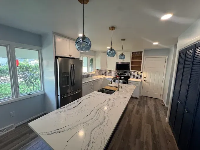 Bright modern kitchen with marble island, stainless appliances, blue cabinets, and pendant lights