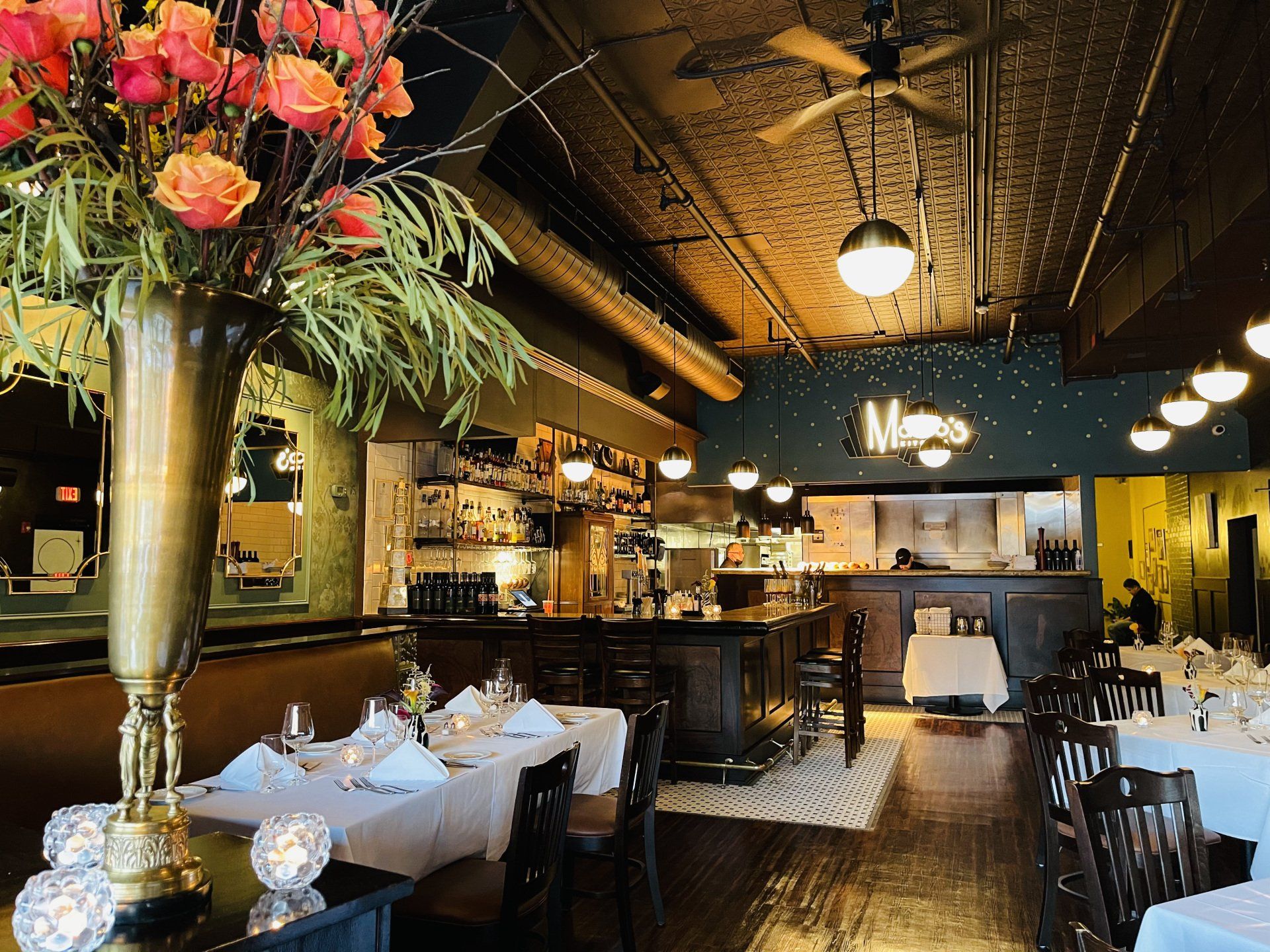 Restaurant interior: tables set with white tablecloths, bar, and floral centerpiece.