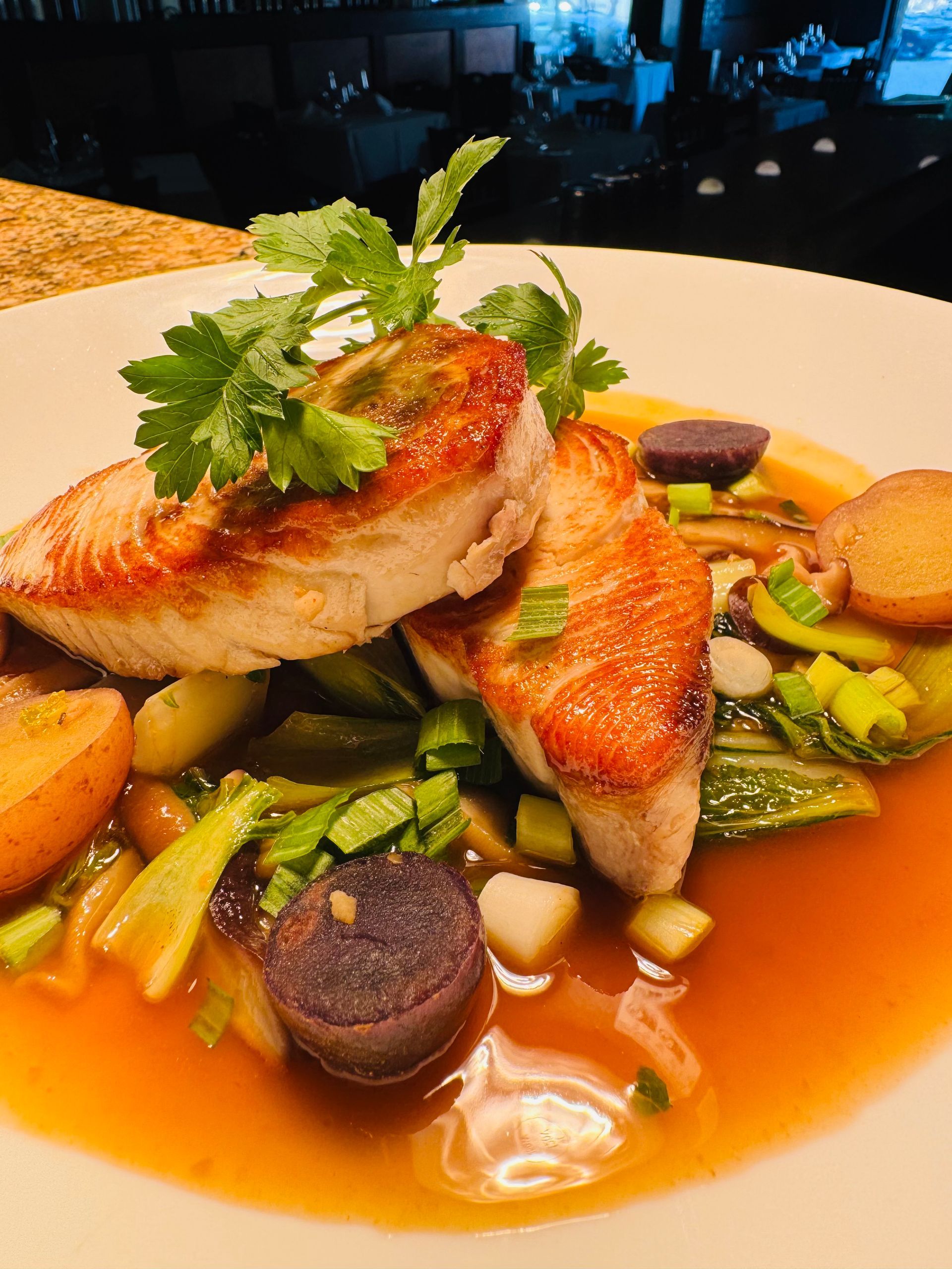 Seared fish fillets on a bed of vegetables and sauce, garnished with parsley.