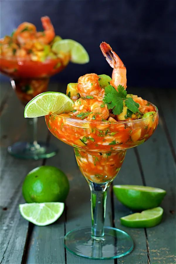 A martini glass filled with shrimp , avocado , cilantro and lime slices.