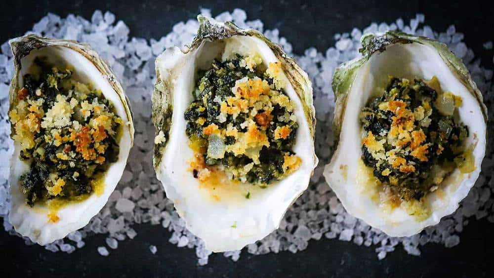 Three oysters are sitting on top of a pile of salt on a table.