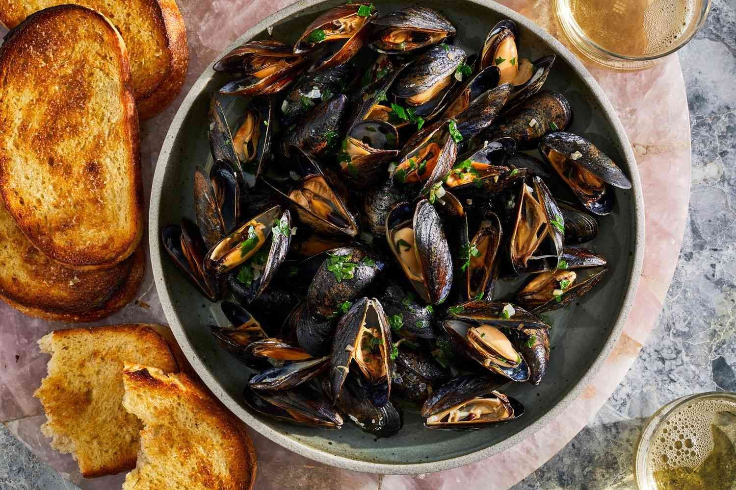 Steamed mussels in a bowl with toasted bread and white wine.
