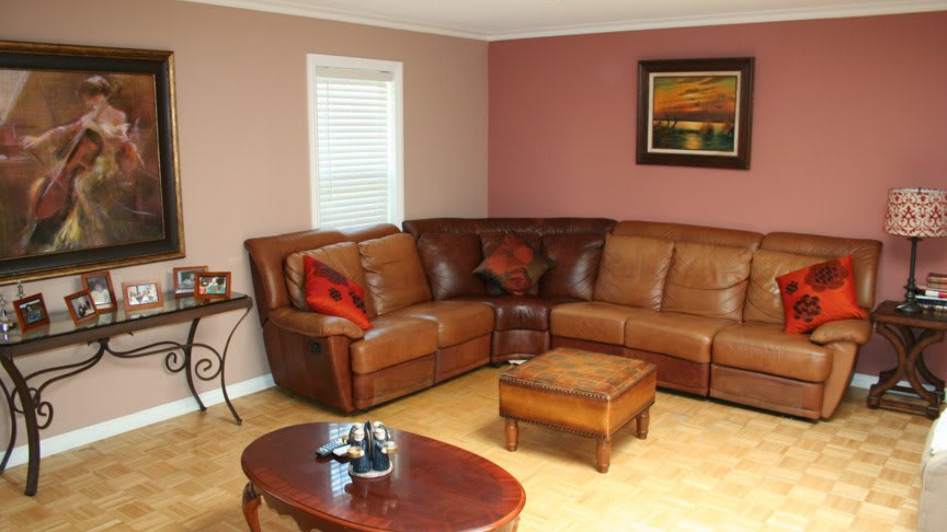 A living room with a large tan leather sectional, a central ottoman, a coffee table, and walls in shades of brown and red.