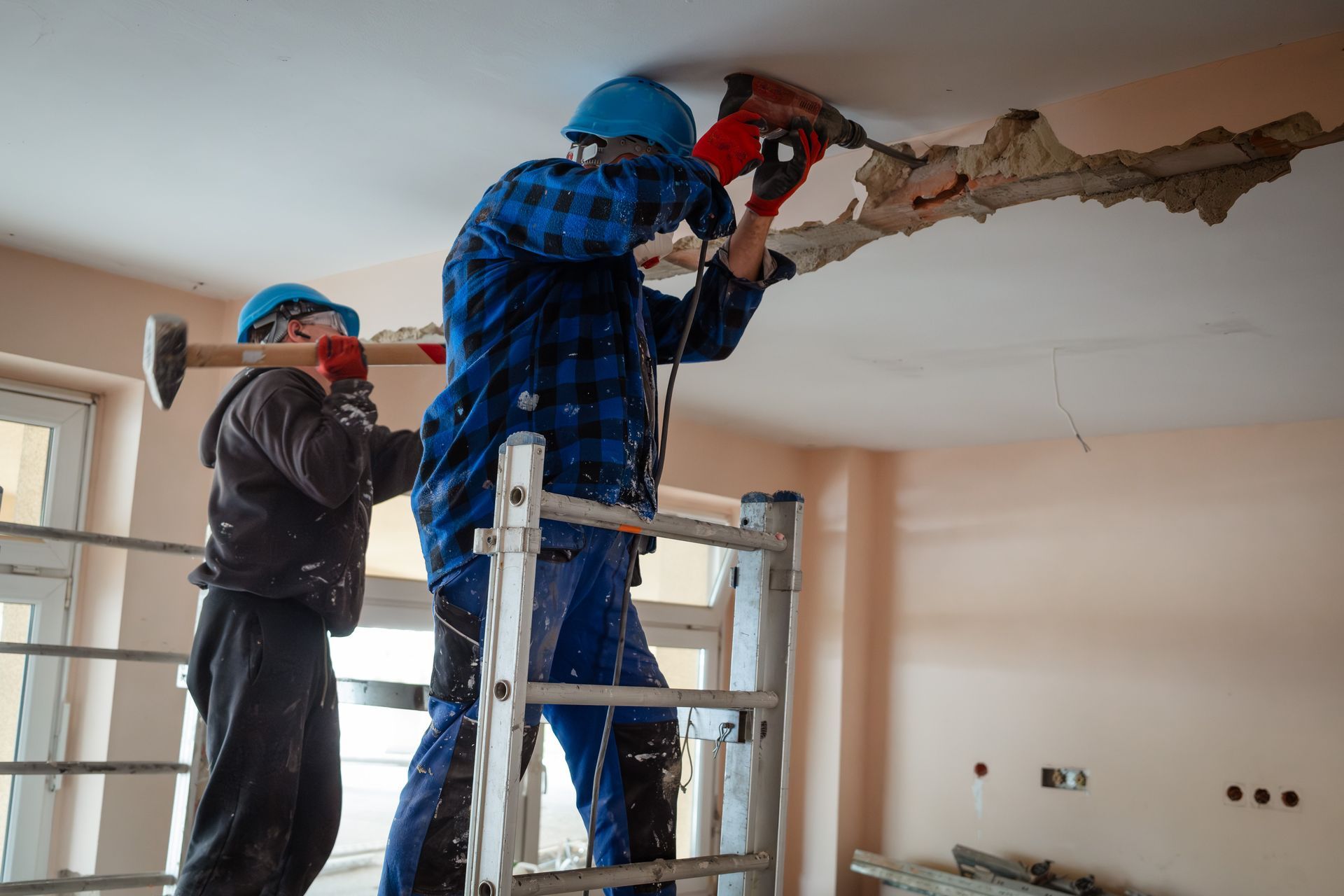 Two builders on scaffolding demolish a wall with a hammer and a drill. Two builders on scaffolding demolish a wall with a hammer and a drill.