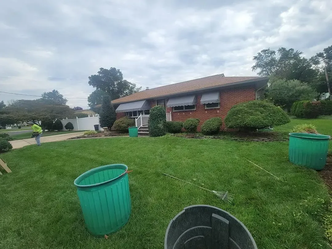 A green trash can is sitting in the grass in front of a house.