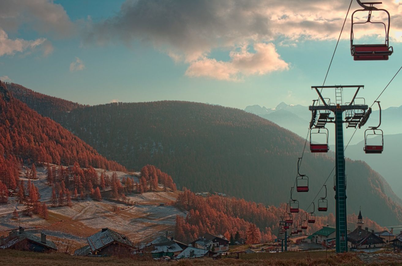 Autumn landscape in Chamois, Aosta Valley, with chairlift, colorful forests, and alpine peaks.