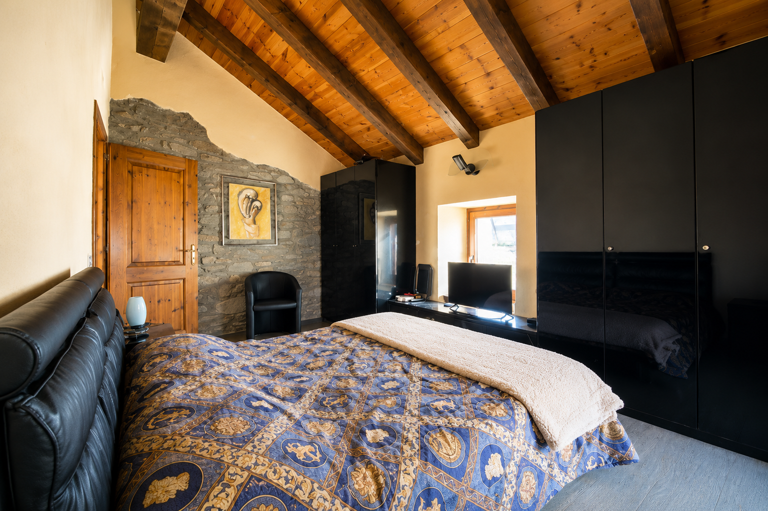 Rustic double bedroom at The Old Barn by Roby with exposed wooden ceiling, natural stone walls and traditional mountain-style furnishings.