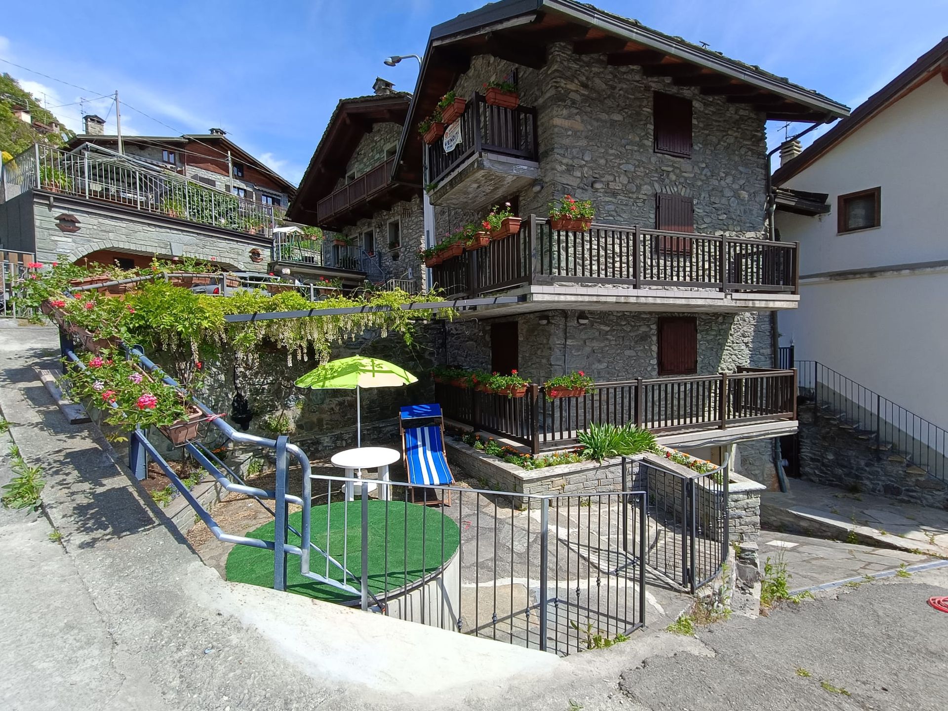 Traditional stone facade of The Old Barn by Roby in the hamlet of Moron, decorated with colorful flowers and typical Aosta Valley architectural details.