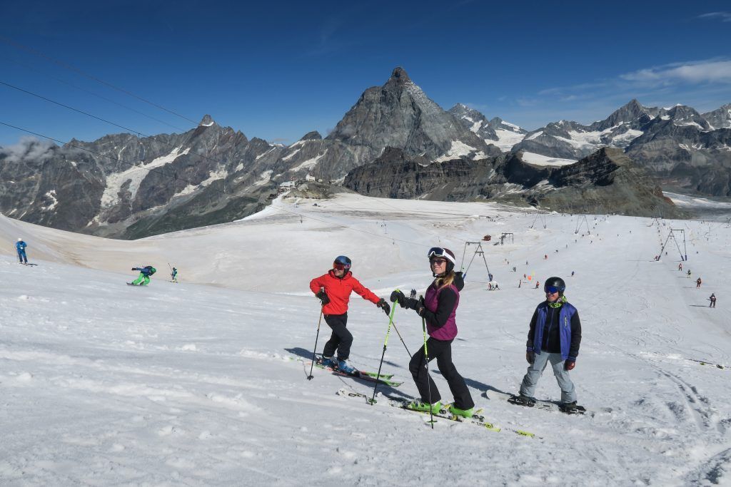 Sciatori in discesa sul ghiacciaio di Cervinia in estate, con vista panoramica sul Cervino