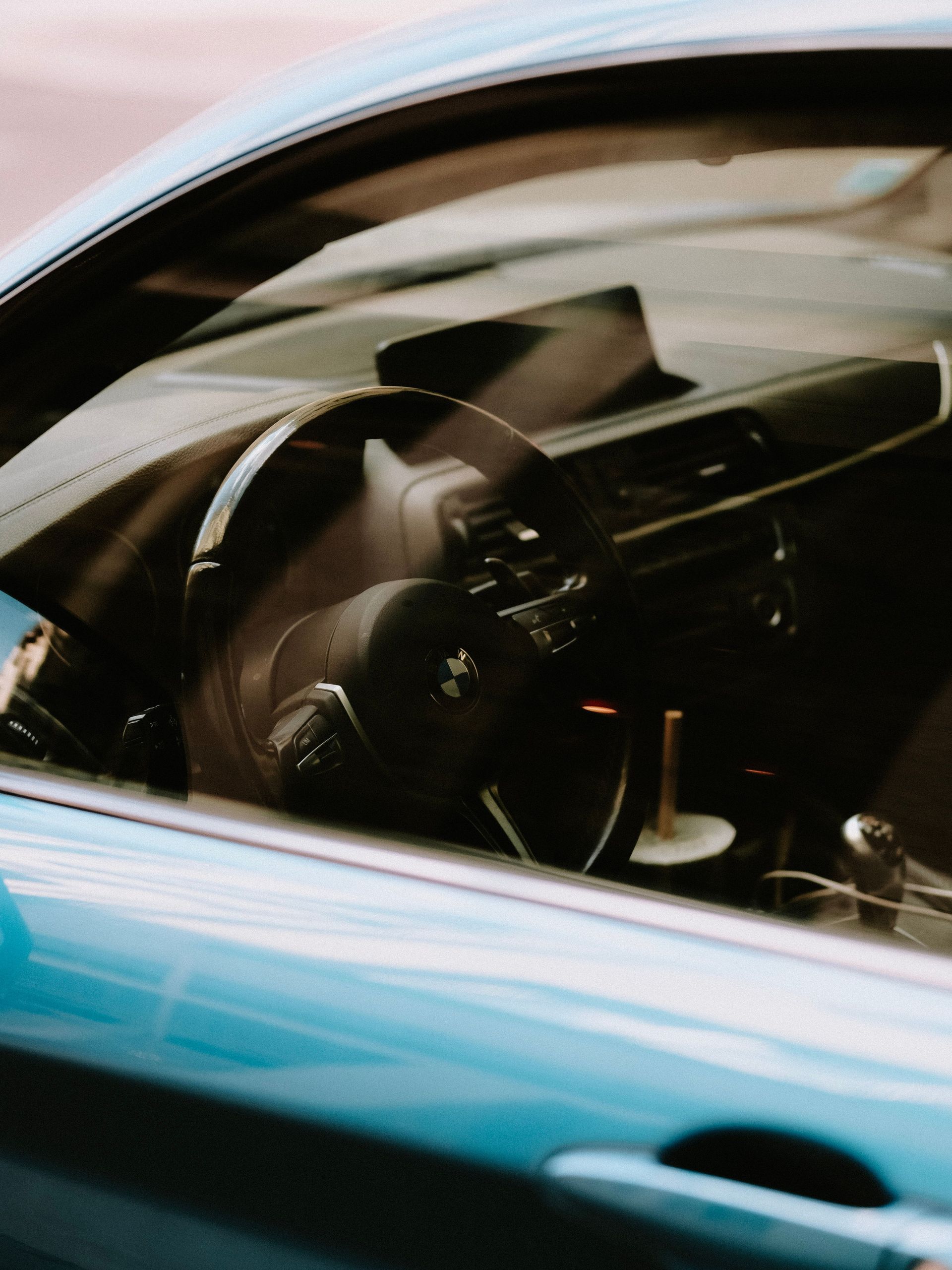 Person driving a teal car, seen through the side window reflection
