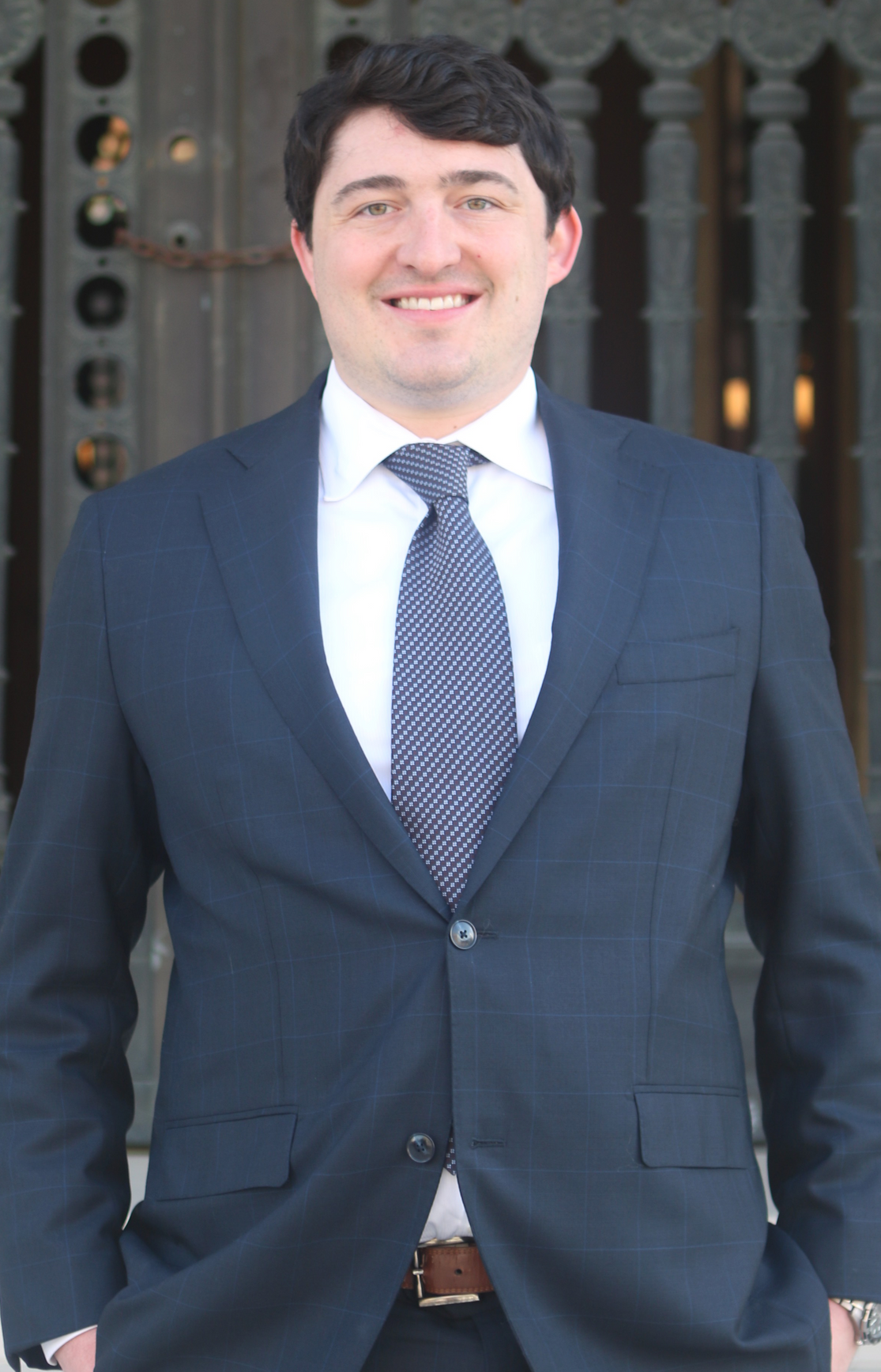 Man in a suit, smiling, standing outside a building with a decorative door.