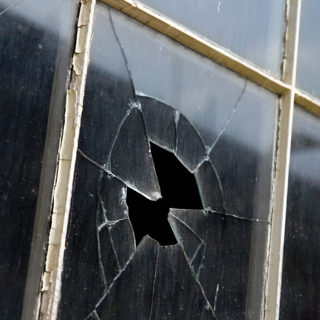 Broken window with a hole, showing cracks, in an old wooden frame.