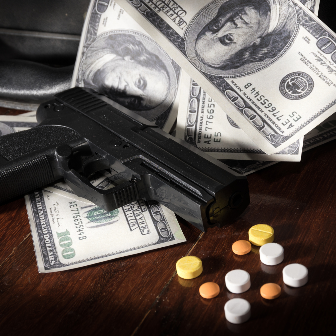 Gun, money, and pills on a wooden surface.