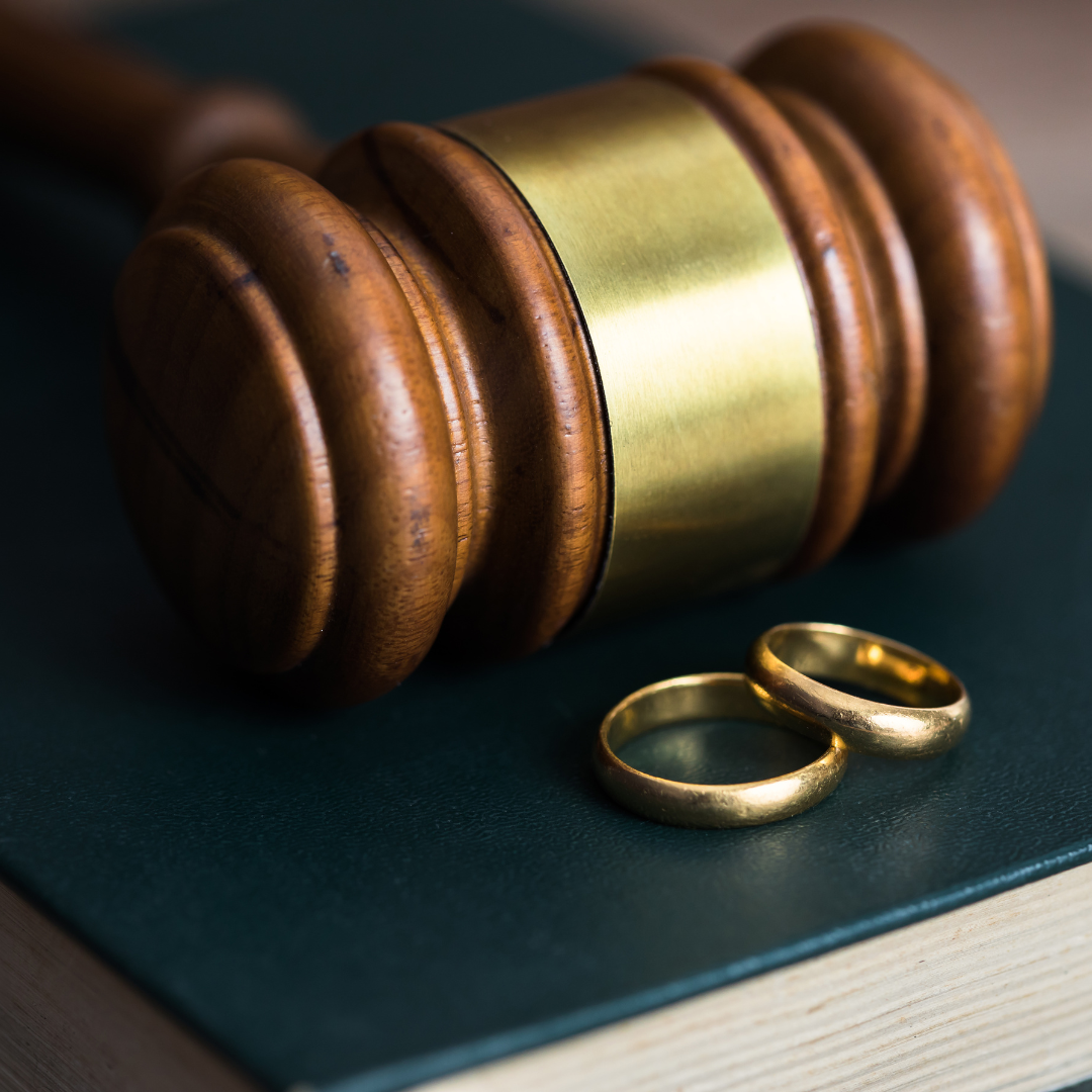 Gavel and wedding rings on a closed book, suggesting divorce or legal proceedings related to marriage.