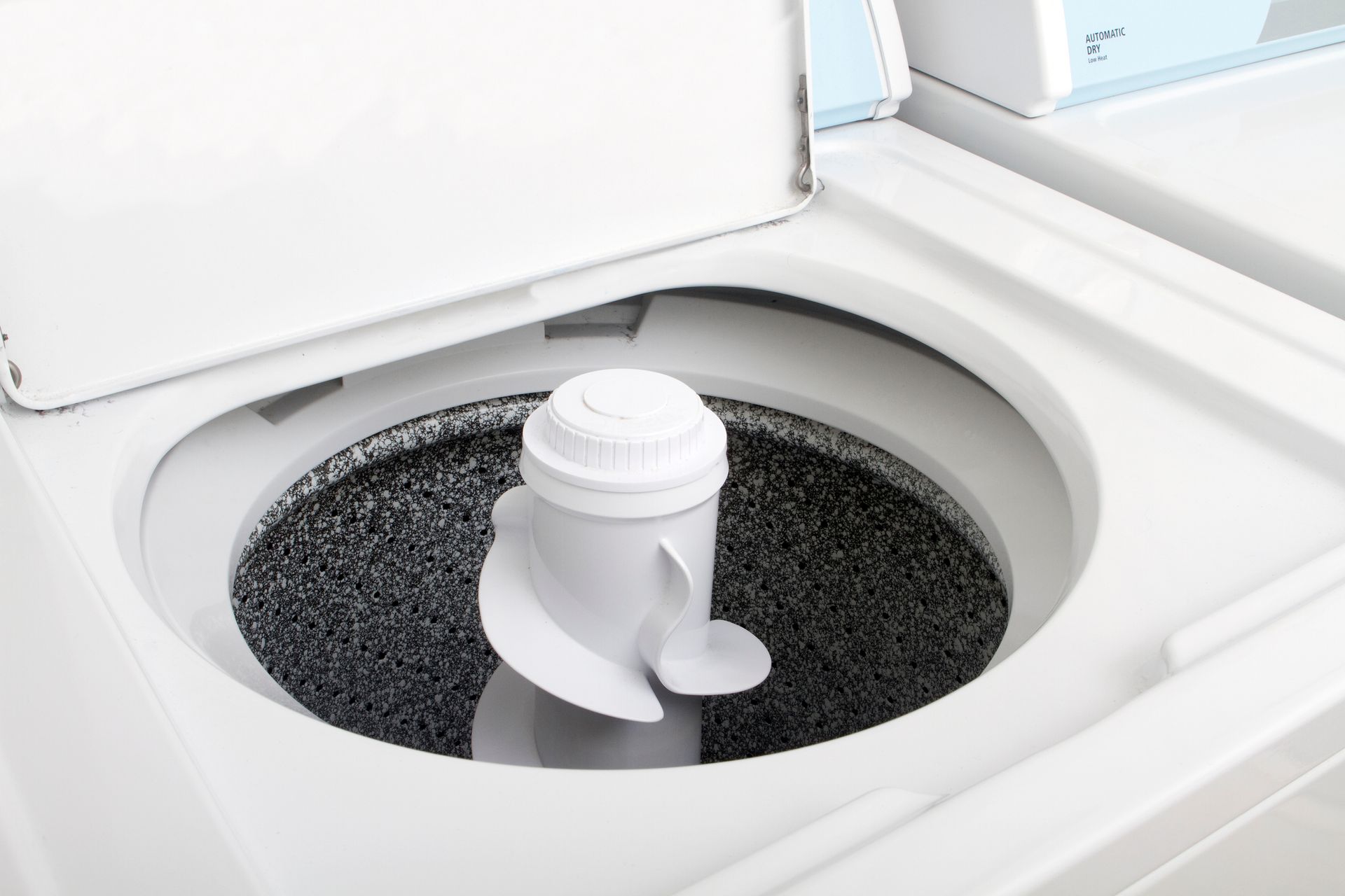 A person's hand touches the inside of a washing machine drum, its front panel open for repair.