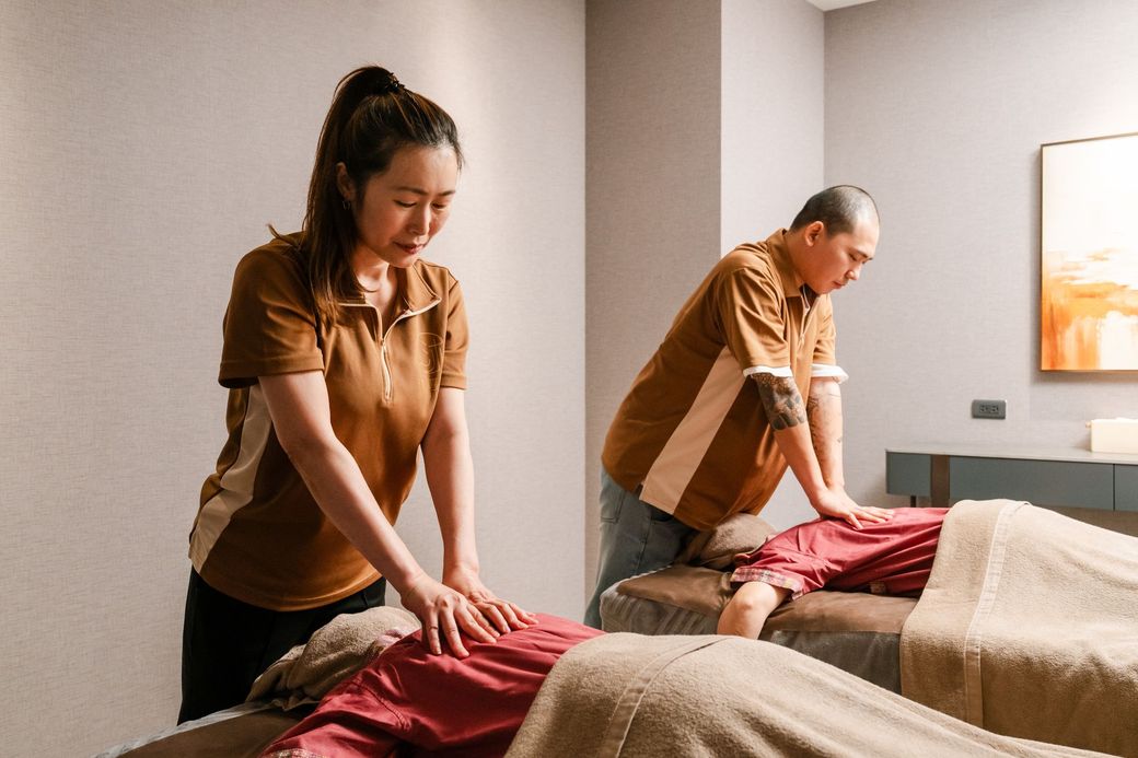 兩名身穿棕色制服的按摩師正在按摩床上為顧客進行背部按摩。