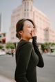 一位身穿黑色上衣的女子在城市街道上微笑，背景中有一棟模糊的建築物。