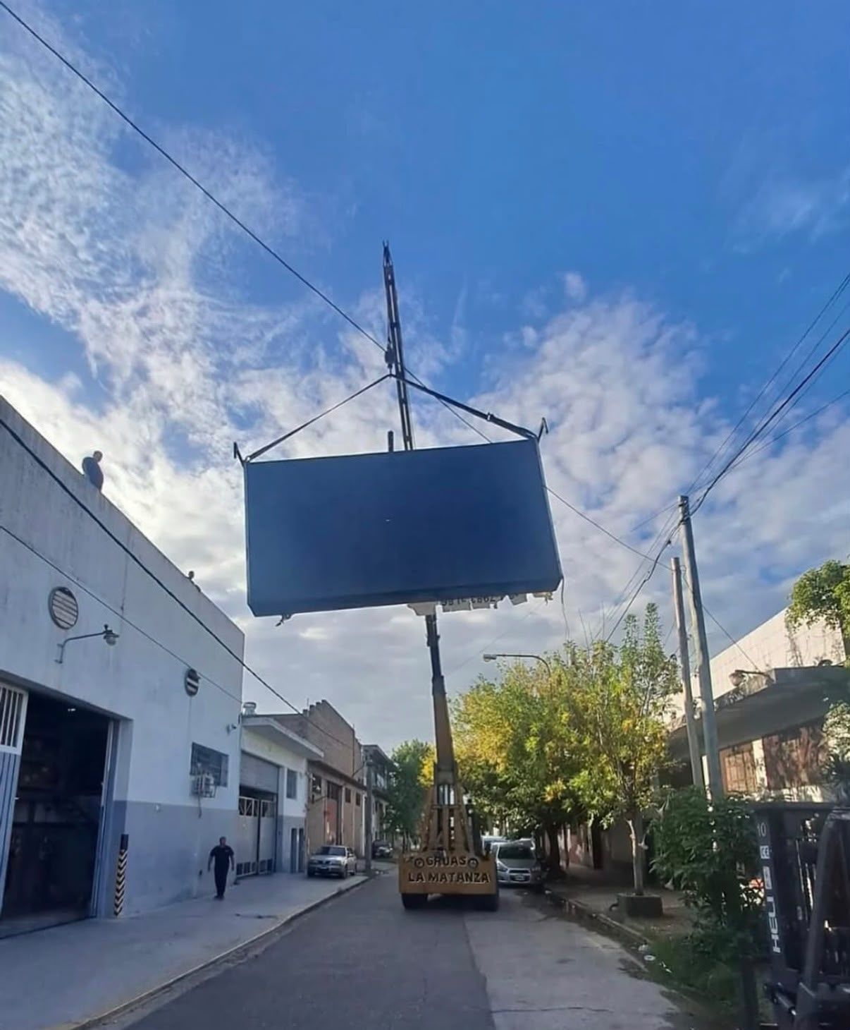 Obra en construcción con grúa levantando un panel de hormigón mientras los trabajadores guían una carretilla elevadora