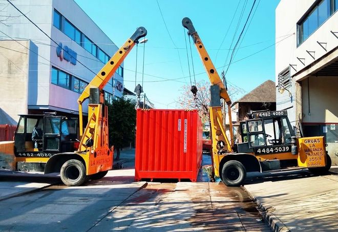 Una carretilla elevadora naranja carga una gran máquina blanca en un camión de plataforma en un patio industrial.