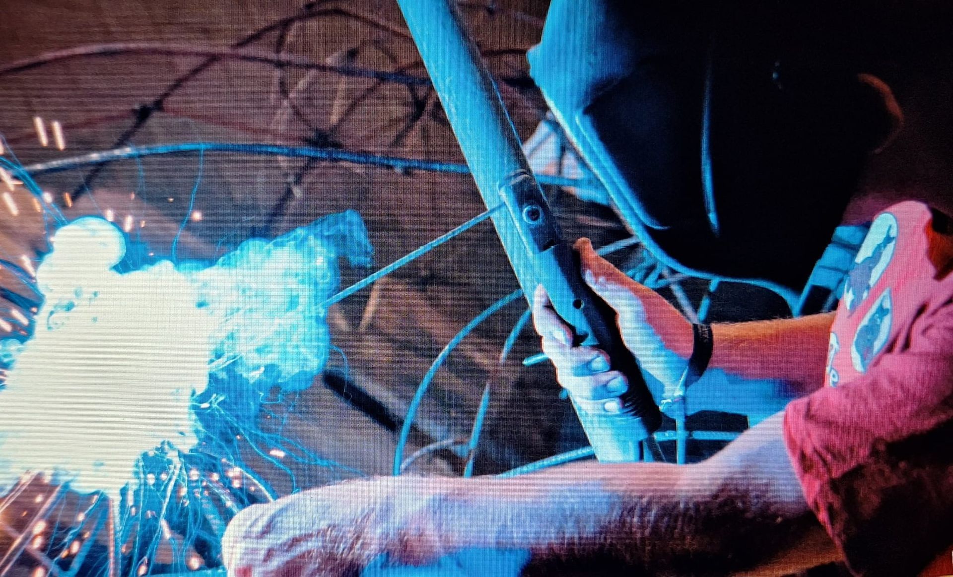 Een arbeider gebruikt een lasbrander; felblauwe vonken verlichten een donkere industriële omgeving.