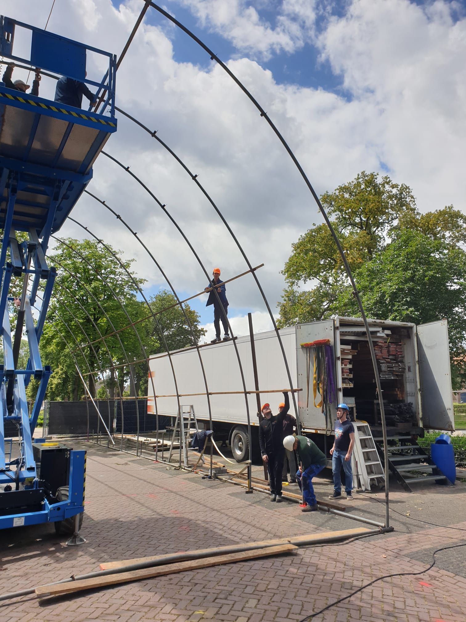 Een arbeider staat op een witte vrachtwagen onder gebogen metalen bogen op een bouwterrein in de openlucht.