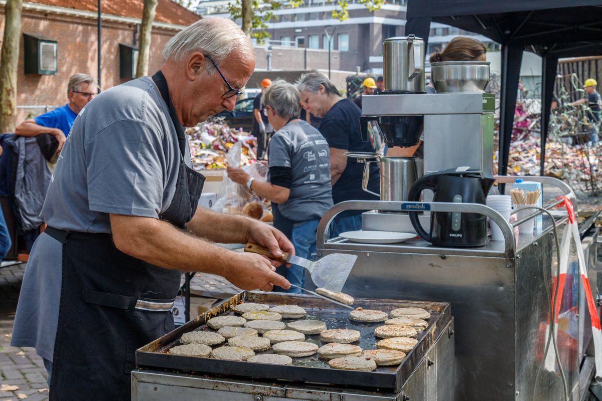 Een man grilt eten op een buitenmarkt, terwijl er rook van de grill opstijgt.