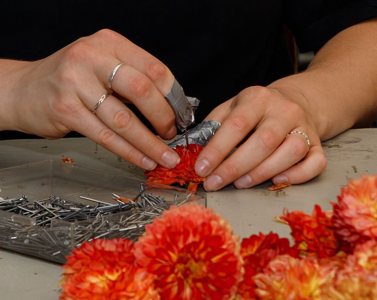 Handen schikken oranje en rode bloemen op een tafelblad naast zilveren sierstelen.