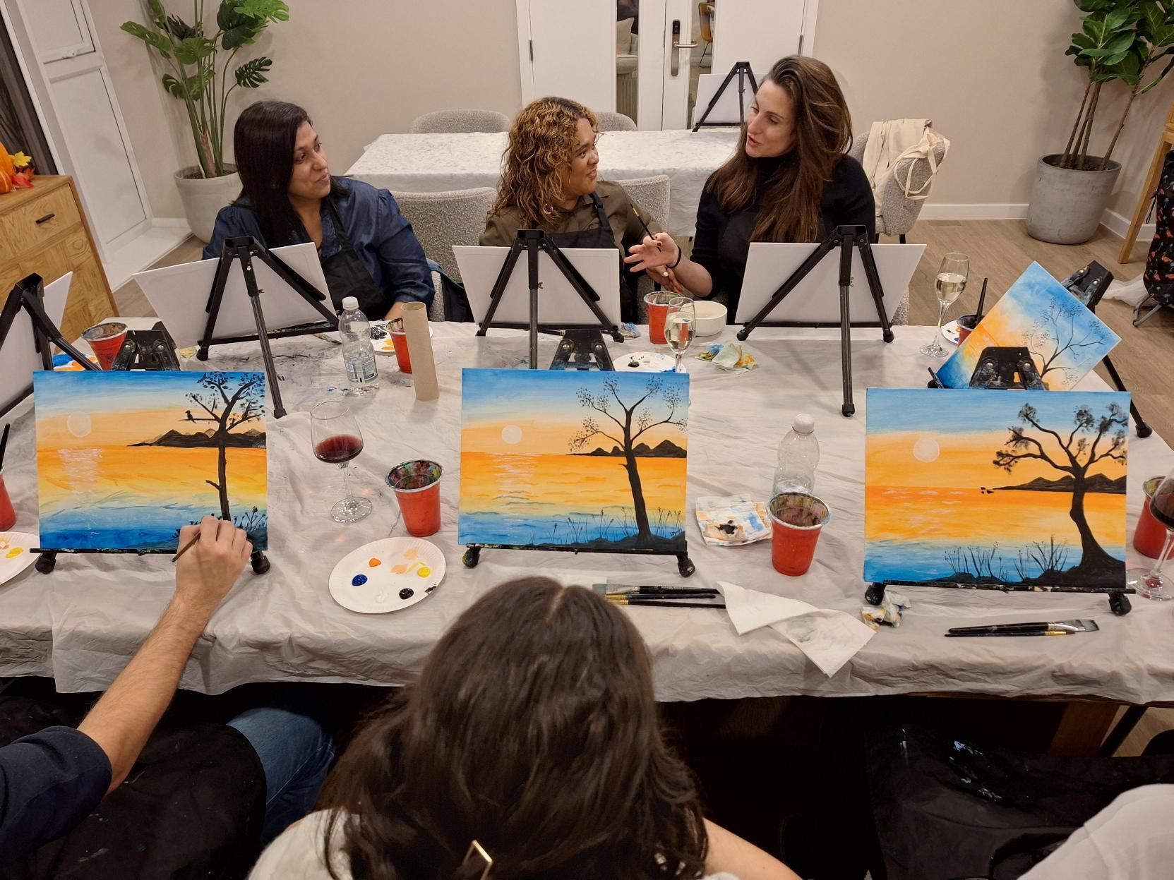 People painting sunset scenes at a table in a bright art studio
