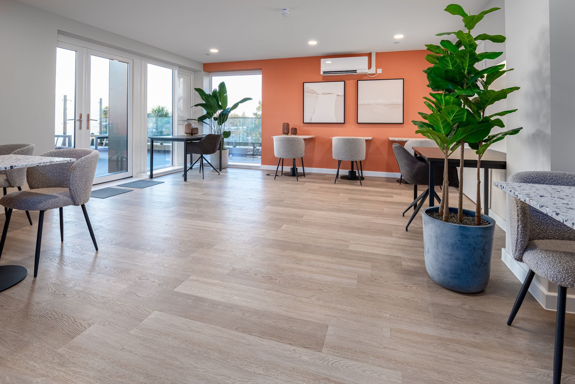 Modern waiting area with orange accent wall, gray chairs, and potted plants on wood flooring