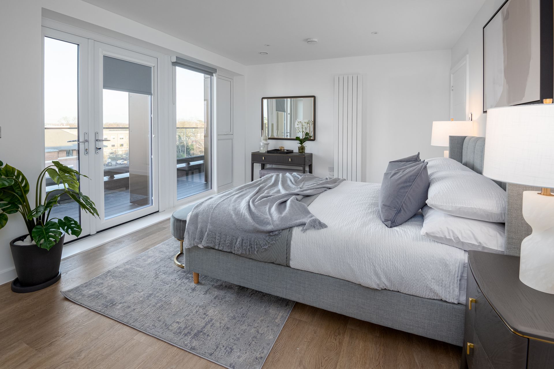 Bright modern bedroom with large windows, gray bed, and light wood floors