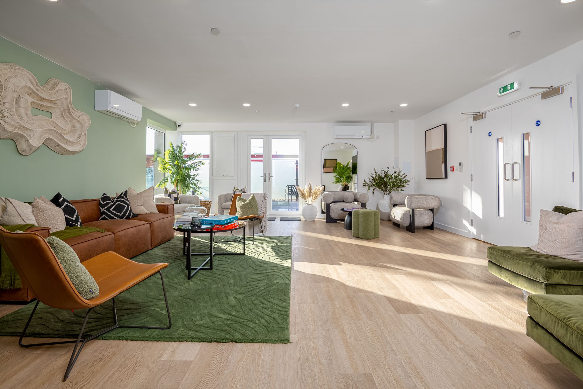 Bright modern living room with orange sofa, green rug, plants, and sunlight from large windows
