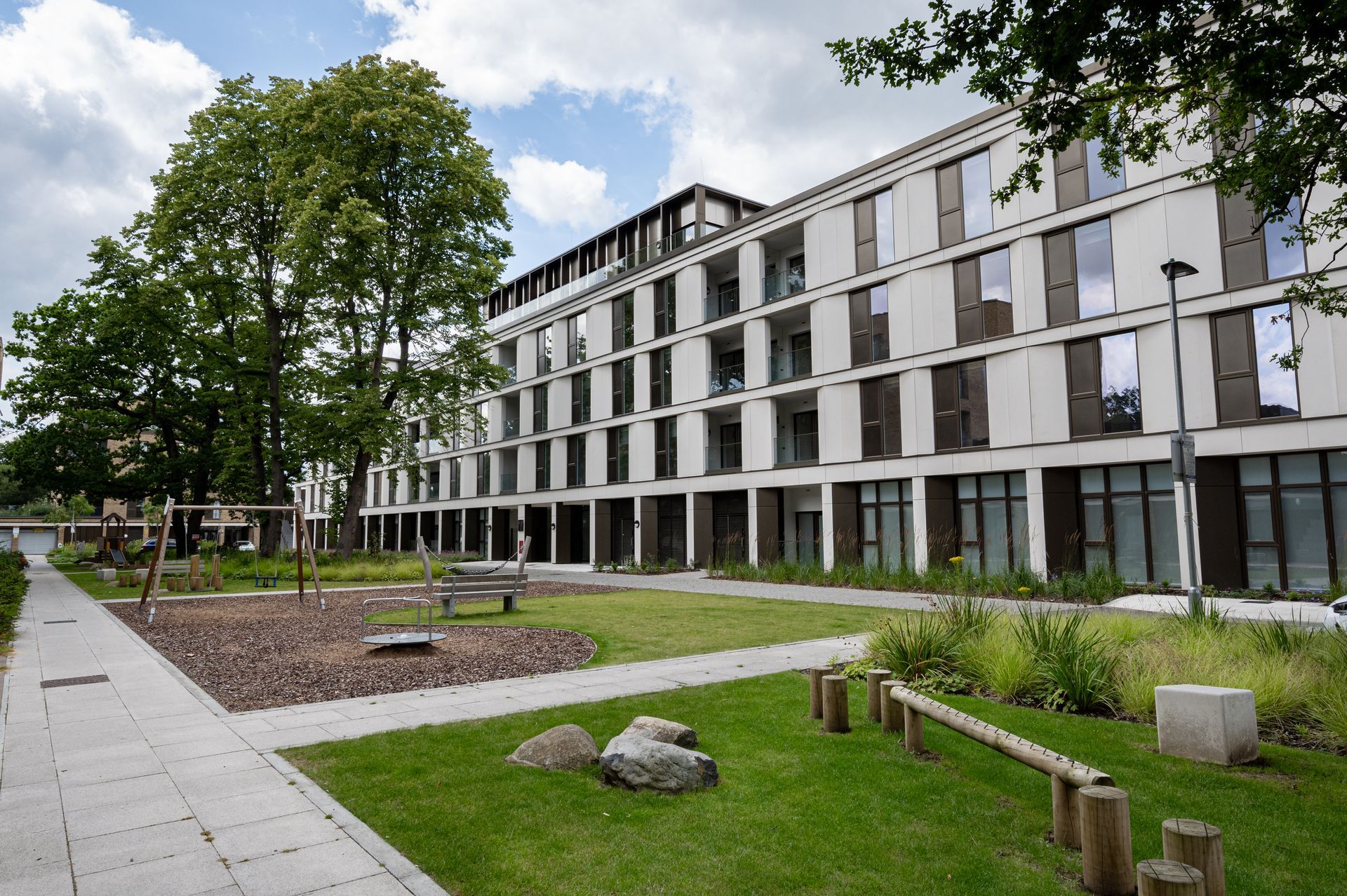 Modern apartment building with a landscaped courtyard, trees, and a walkway