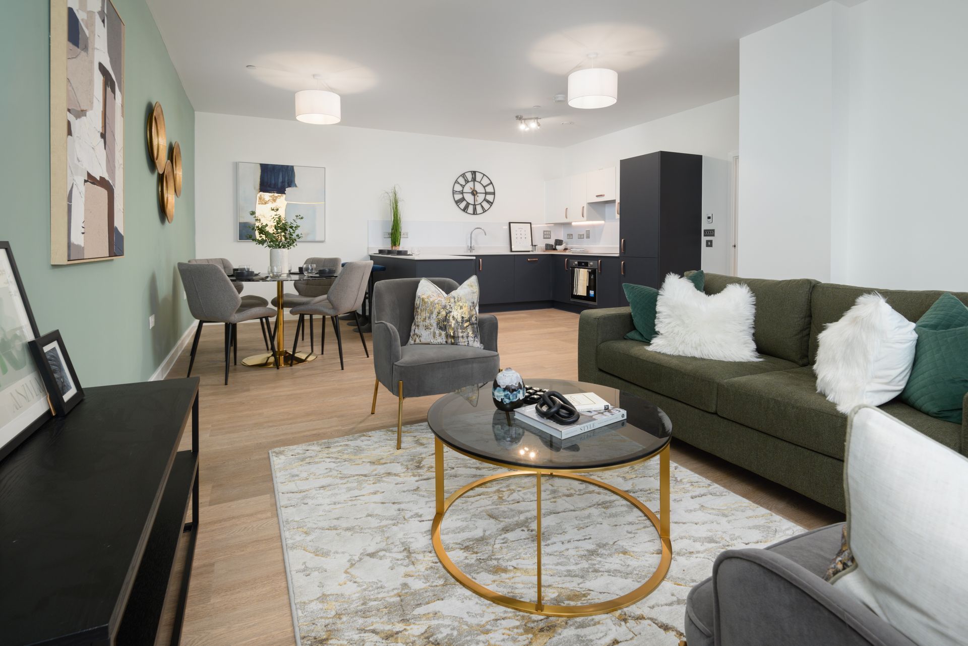 Modern living room with green sofa, round coffee table, dining area, and kitchen in the background