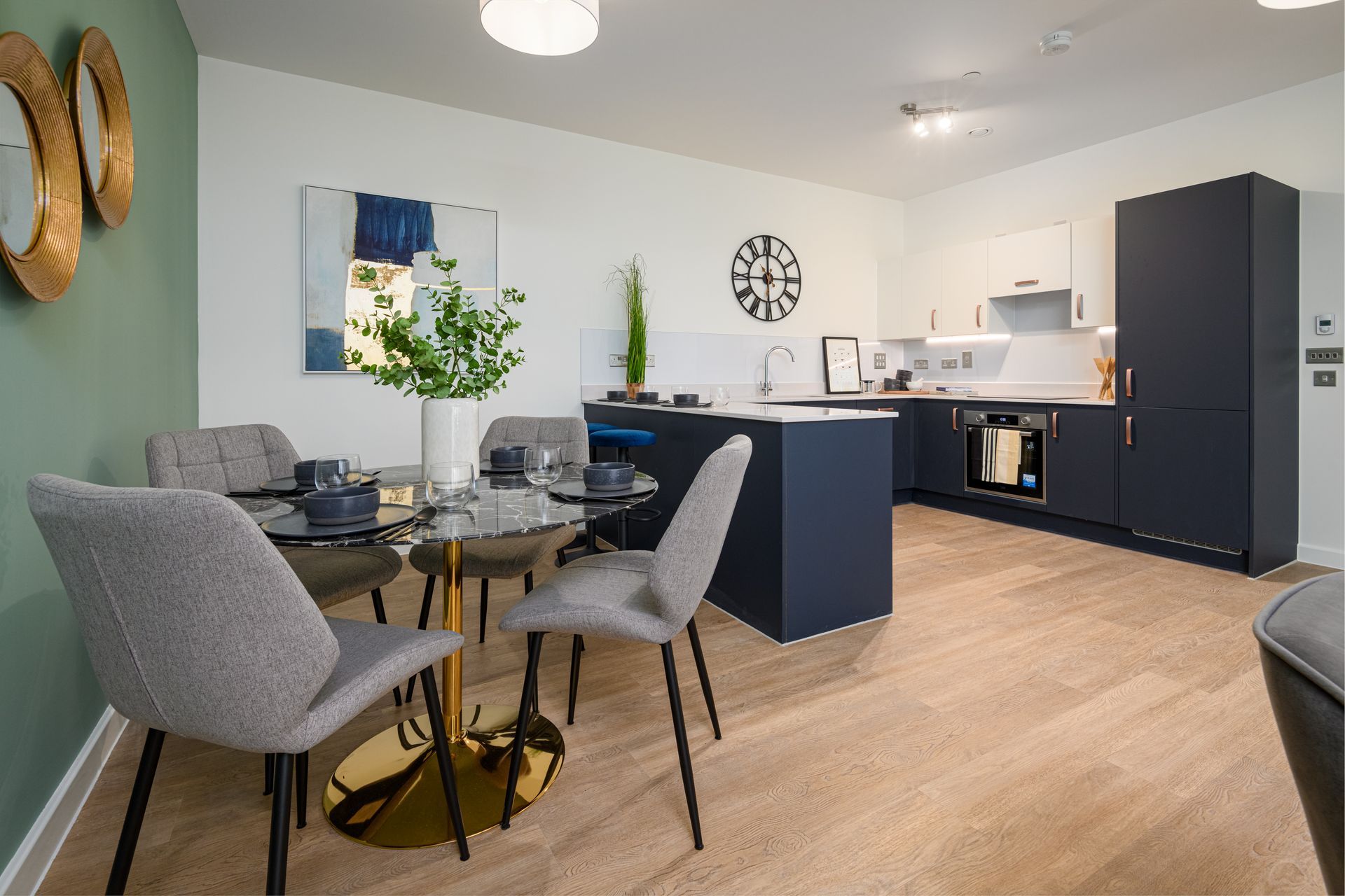 Modern open-plan kitchen and dining area with gray chairs, blue cabinets, and light wood flooring