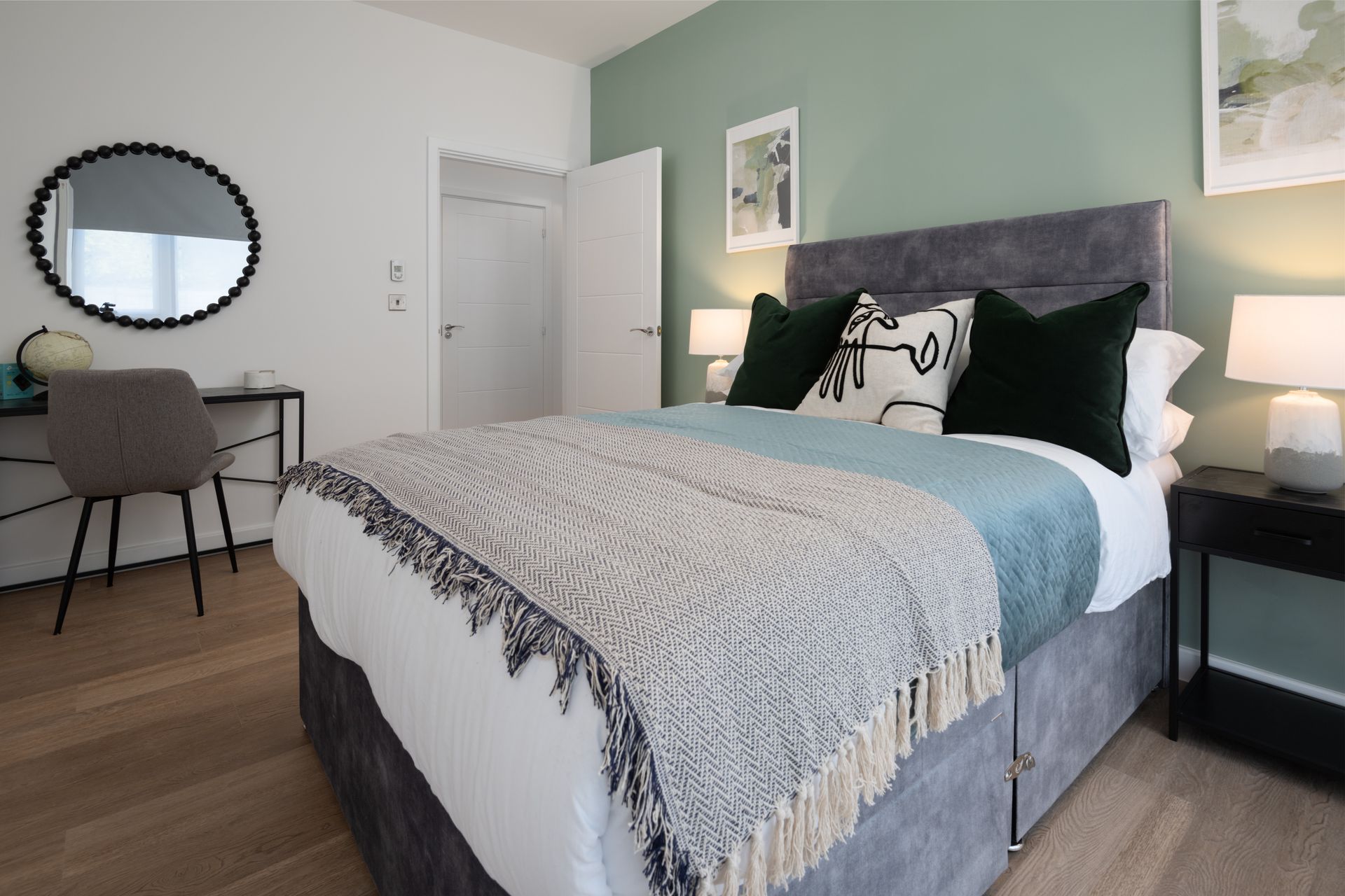 Modern bedroom with gray bed, teal accent wall, desk, round mirror, and bedside lamp
