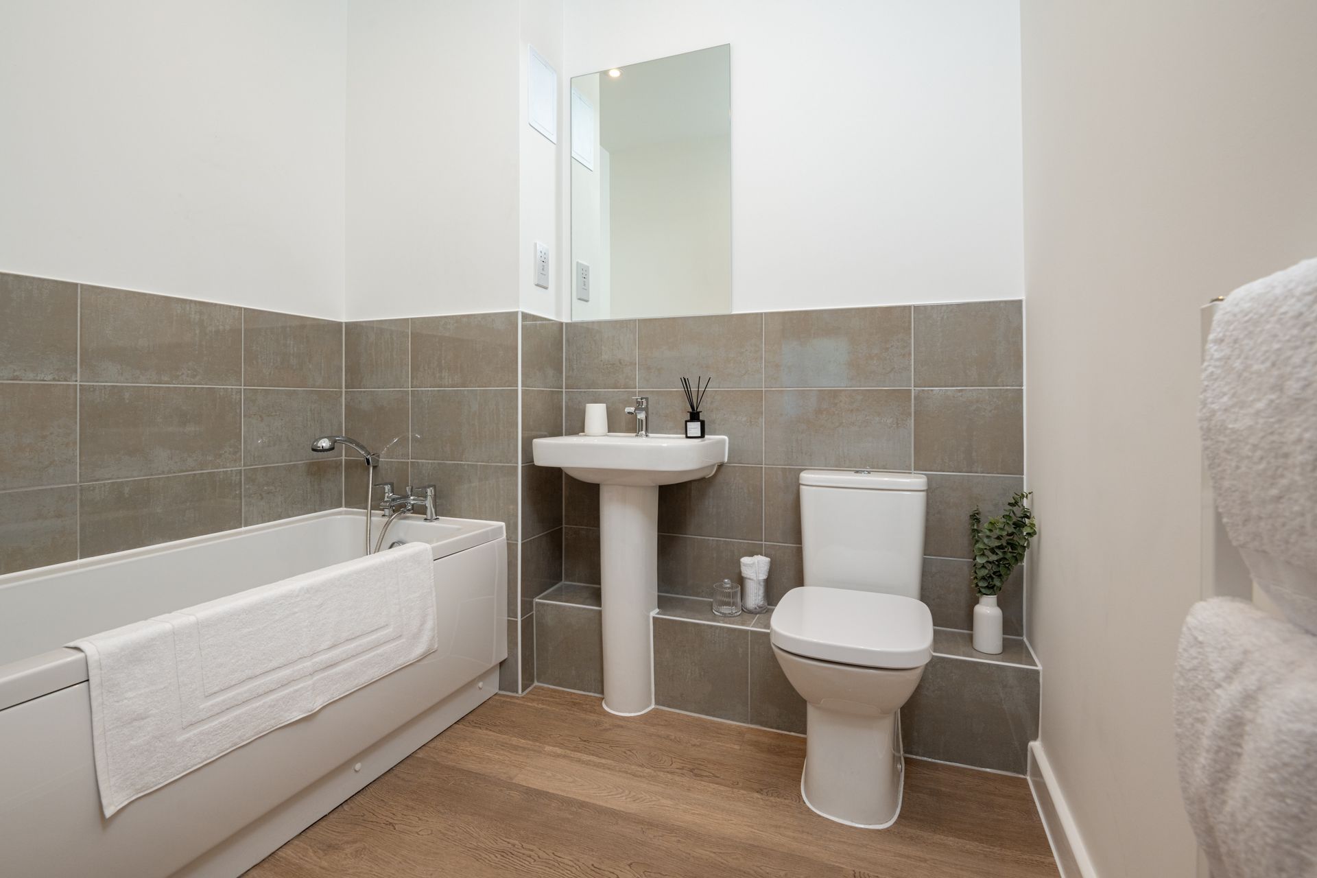 Small modern bathroom with tub, pedestal sink, toilet, and gray tile walls