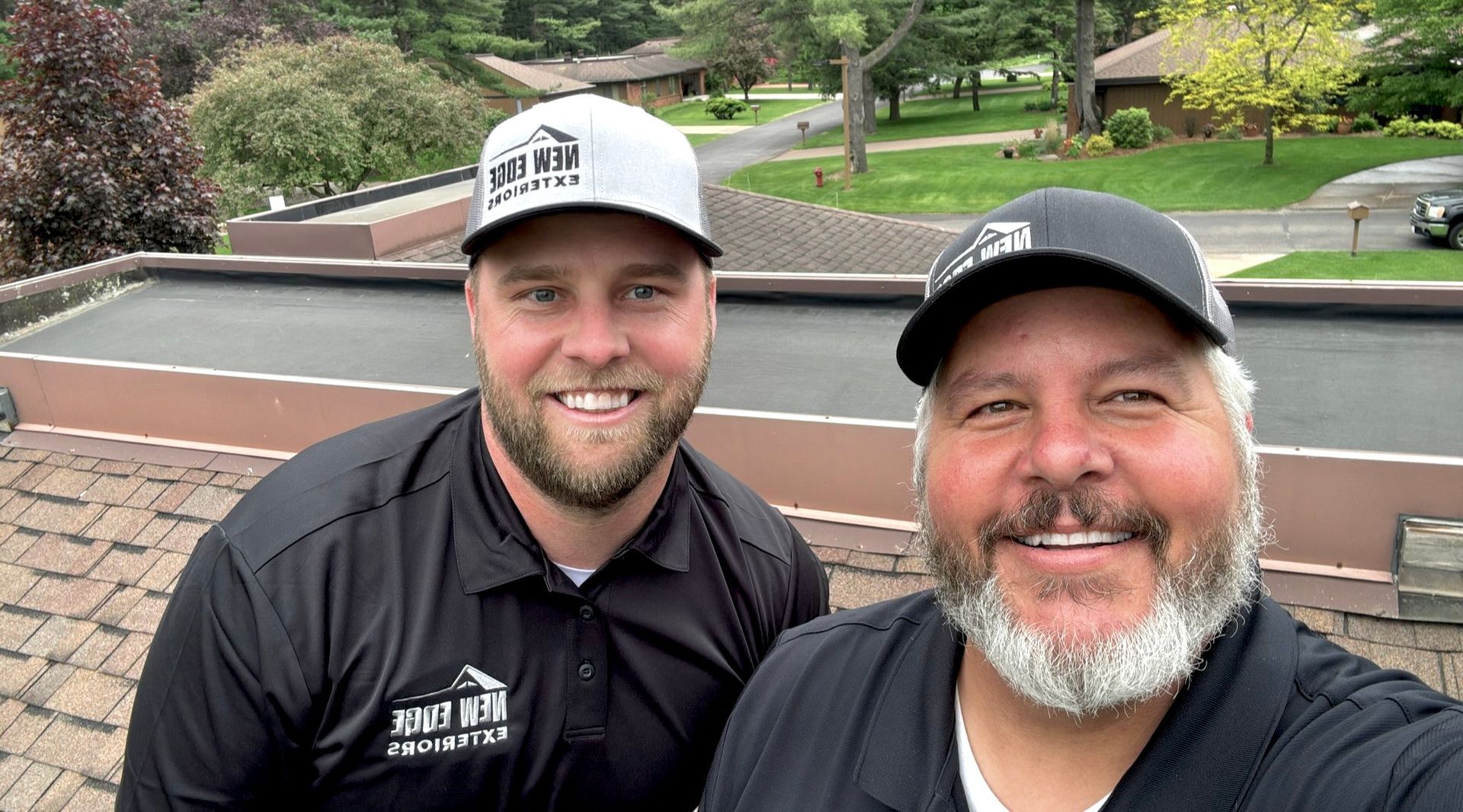 Two smiling men on a rooftop with trees and houses in the background